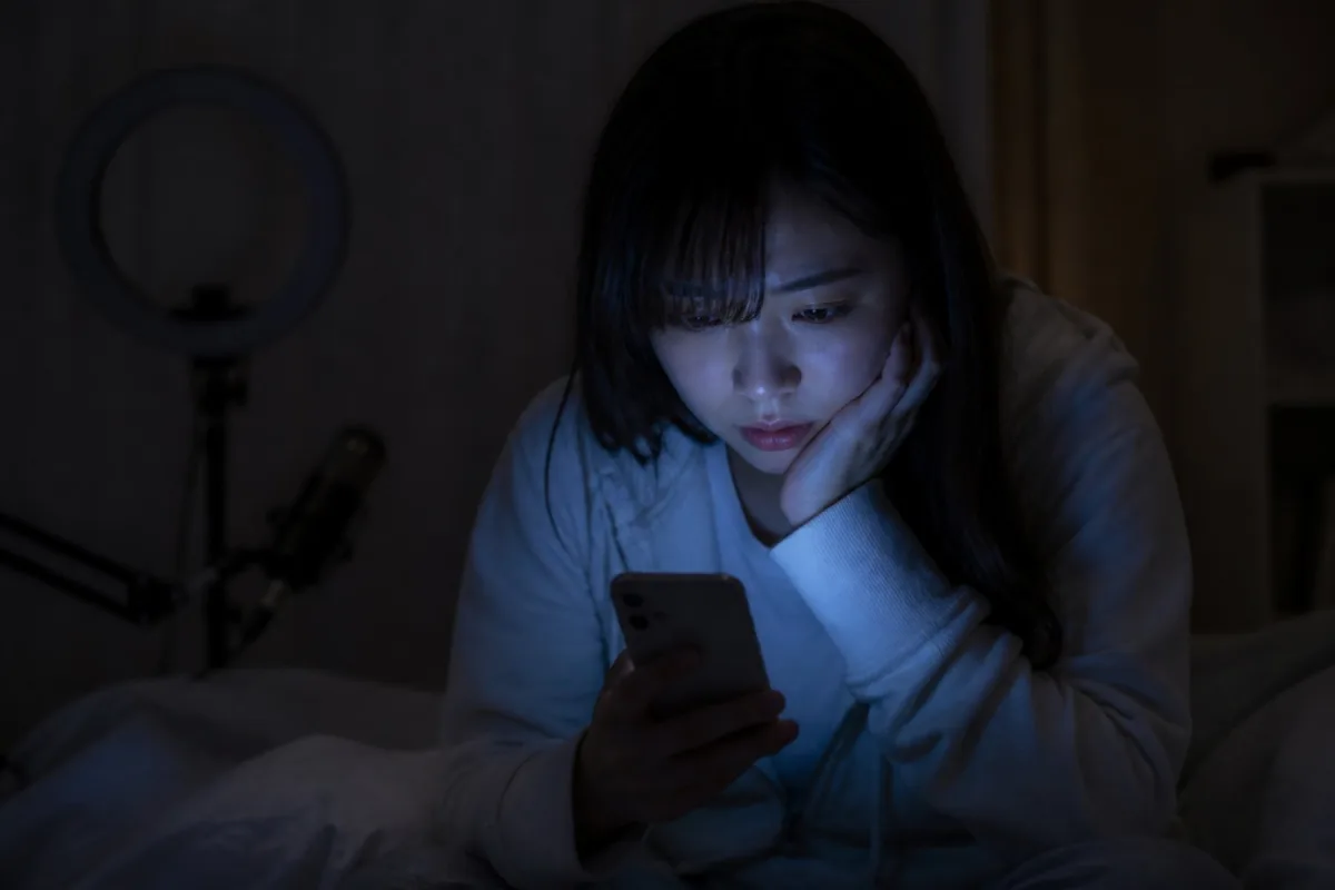 夜の部屋で、スマホを見つめて疲れた様子のライバー